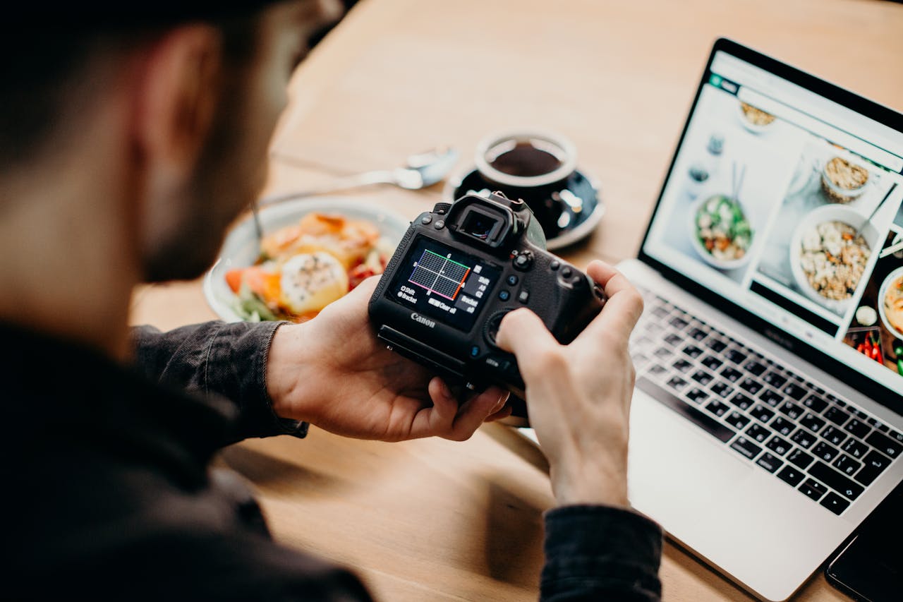 creative A man reviews photo settings on a camera while working on a laptop in a cozy workspace.